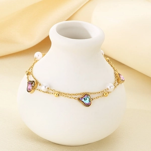 18K gold heart anklet with colorful gemstones and pearls draped on a white ceramic vase