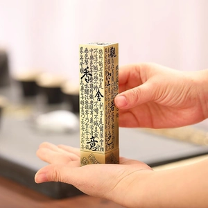 Macro detail of vertical incense burner with engraved Heart Sutra on matte gold surface