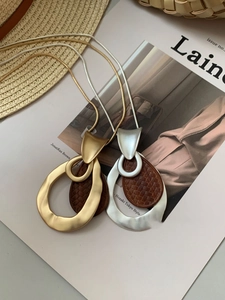 Detail of geometric metal pendant necklace with woven leather texture on a stylish magazine