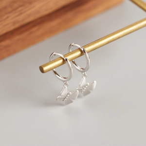 Macro shot of S925 sterling silver hoop earrings with delicate butterfly charms on a metal rod