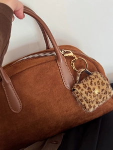 Close-up of brown suede handbag featuring leopard print fur pendant and metal hardware