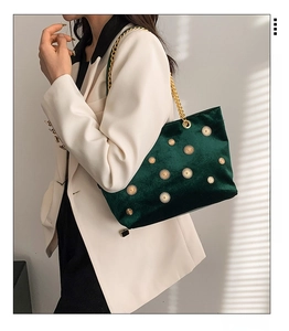 Detail of dark green velvet shoulder bag featuring golden sunburst studs and chain strap