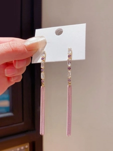 Detailed shot of long gold earrings with purple cubic zirconia and pink chain tassels