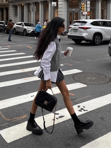 Women's V-neck knit vest layered with white shirt and pleated skirt in street style