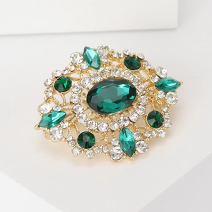 Detail of vintage gold brooch with large green oval gemstone and sparkling crystal accents