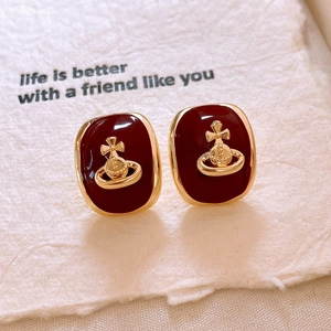 Detail of red enamel heart earrings with gold saturn logo on textured paper background