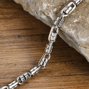 Close-up of silver stainless steel chain link bracelet resting on a grey stone texture