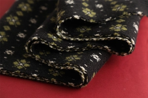 Close-up of black knitted scarf featuring green and white reindeer snowflake patterns