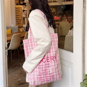 Close-up of pink checkered canvas tote bag with red grocery text in a cafe setting