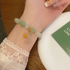 Detail of jade-style beaded bracelet with peanut pendant and green flower charm on wrist