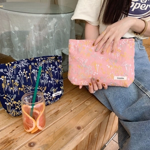 Close-up of floral embroidery detail and brand label on a portable cotton linen makeup bag