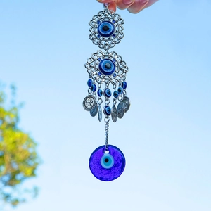Blue Turkish evil eye palm charm with glass pendant and metal bells against a sky background