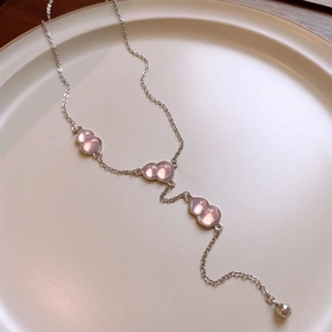 Macro detail of Y-shaped silver necklace with three pink gourd charms in ceramic bowl