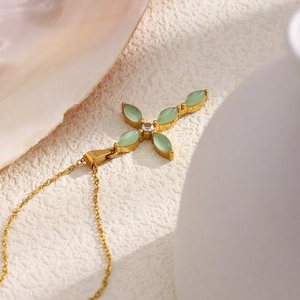 Détail du pendentif croix dorée avec pierres vertes sur une surface texturée blanche