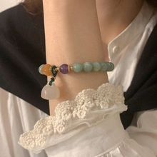 Detail of colorful jade beaded bracelet with a white lucky pouch charm on a wrist