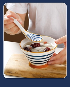 Close-up of hand holding a blue striped ceramic spoon with soup in a matching bowl