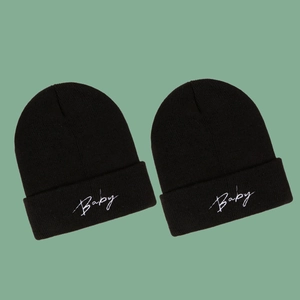 Winter knitted black beanies with Baby embroidery set on green background