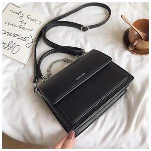 Detail of black leather handbag with silver chain on white bedding with coffee cup