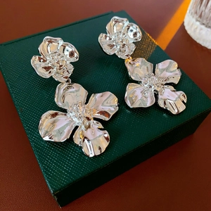 Close-up of silver flower drop earrings displayed on a dark green jewelry gift box