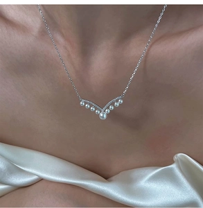 Detailed close-up of a silver V-shaped pearl necklace with zircon accents on silk