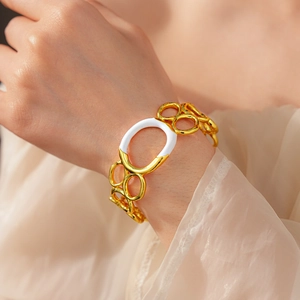 Detail of gold chain bracelet with white oval ring pendant worn on female wrist