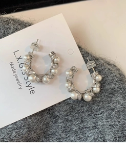 Macro detail of C-shaped pearl earrings with cubic zirconia on a white card display