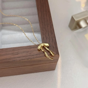 Detailed close-up of a golden bow pendant necklace resting on a velvet jewelry box
