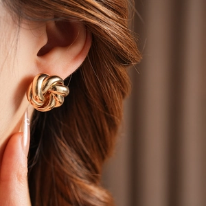 Close-up of a gold knot swirl earring worn by a model showcasing its polished metal texture
