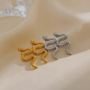 Macro shot of gold and silver snake earrings with scale textures on beige fabric