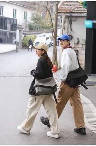 Street view of a large canvas messenger bag in black and grey-green for daily use