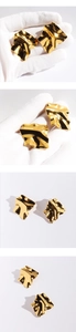 Macro detail of golden irregular wavy mirror-finish stud earrings held in hand