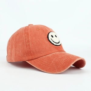 Detail of rust red washed cotton baseball cap with chenille smiley face patch