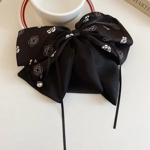 Détail de la pince à cheveux noeud en satin noir avec imprimé camélia et perle