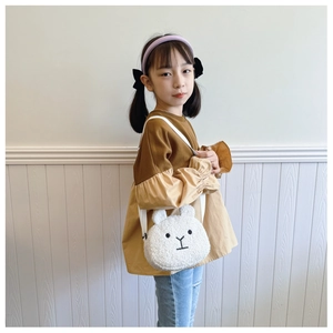 Detail of a white plush bunny shoulder bag shown on a young girl in a soft indoor setting