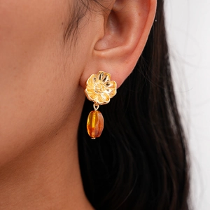Close-up of elegant gold flower earrings with amber resin beads worn by a model