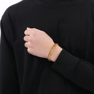 Detail view of double-layered gold Cuban and paperclip chain bracelet on male model sleeve