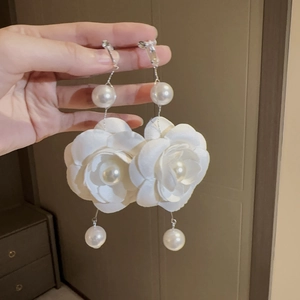 Macro detail of large white fabric flower earrings with layered petals and faux pearls