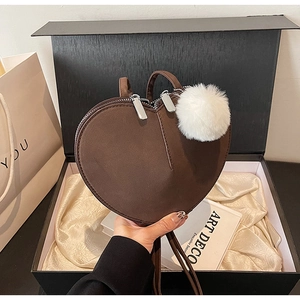 Nahaufnahme der braunen herzförmigen Tasche mit Plüsch-Anhänger in einer edlen Geschenkbox