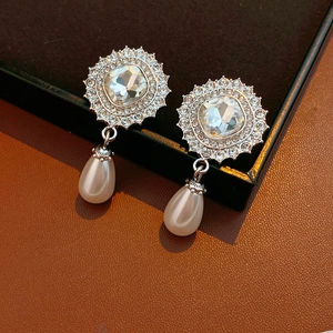 Detailed view of silver drop earrings with white pearls and crystals on a jewelry box