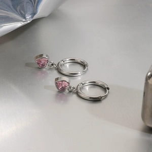 Detail van zilveren oorringen met hartvormige roze zirkonia hangers op een metalen achtergrond