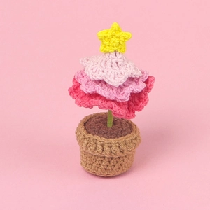 Gros plan d'un sapin de Noël au crochet rose avec étoile jaune et pot de fleurs