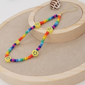 Colorful beaded phone charm with yellow smiley faces and golden clasp on a wooden stand
