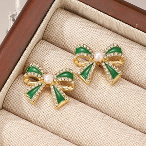 Detailed macro view of green enamel bow earrings with white rhinestones and a central pearl