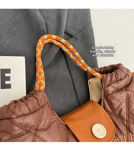 Detail of quilted brown tote bag with orange and blue braided rope handle and leather flap