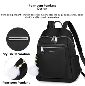 Close-up of black backpack detail featuring white fur ball charm and metal bar hardware