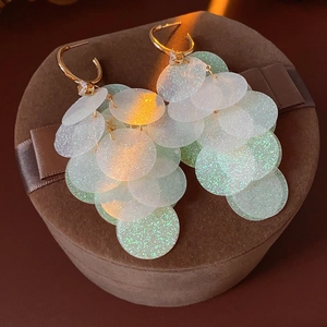 Detailed close-up of gold tassel earrings with sequins on a brown jewelry box