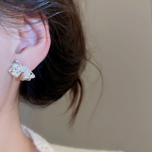 Elegant bow-shaped silver stud earrings with zircon crystals worn by a model on ear