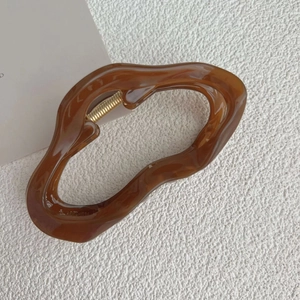 Detail of irregular brown resin hair claw clip with golden metal spring on light texture