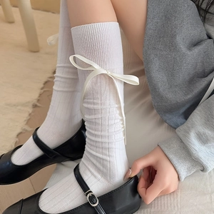 Close-up of white ribbed calf socks featuring silk ribbon bows and vertical textures