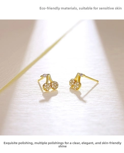Macro detail of gold cherry stud earrings with micro-set zircon stones on textured surface